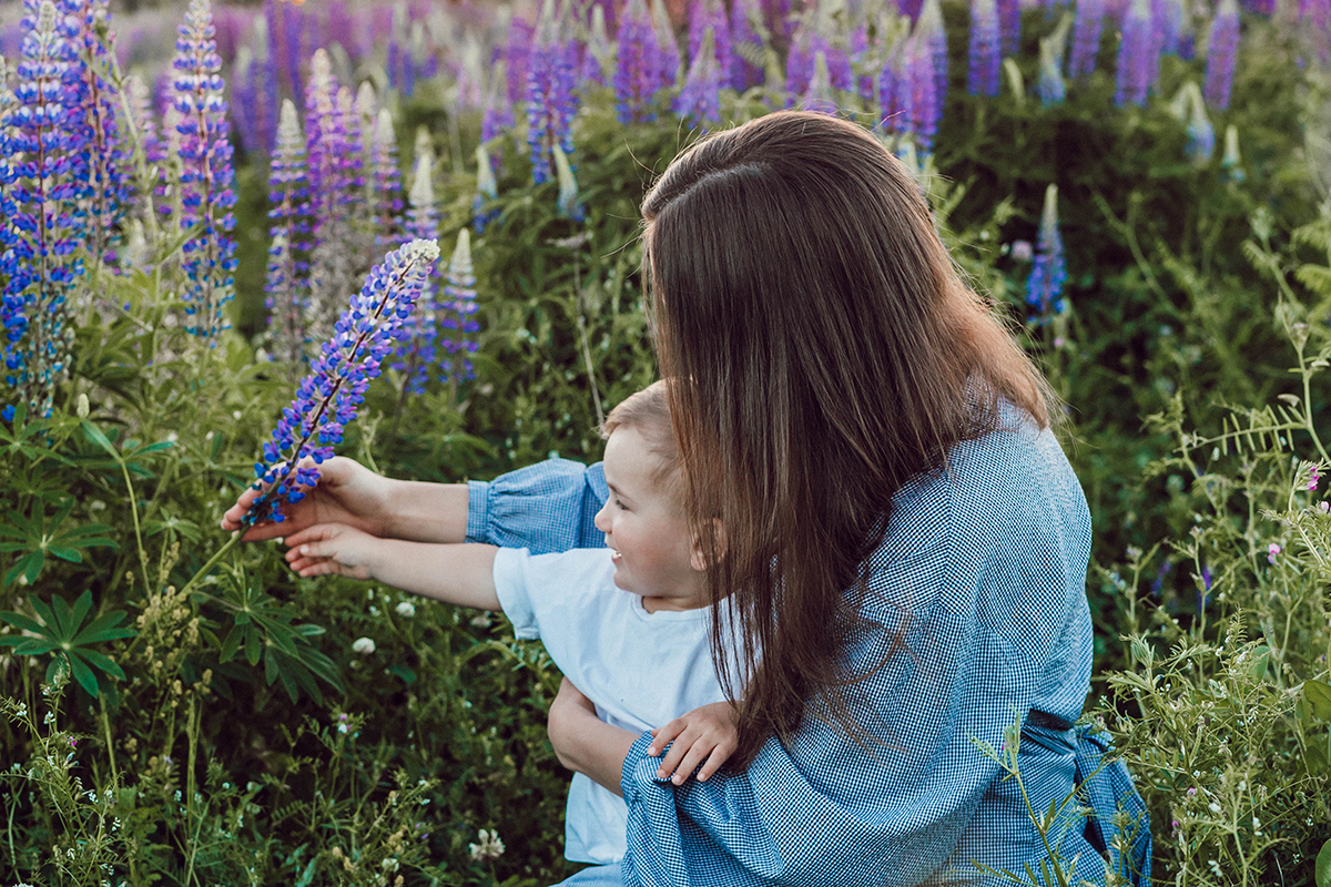 Eine Mutter sitzt mit einem Kleinkind in einem Blumenfeld.