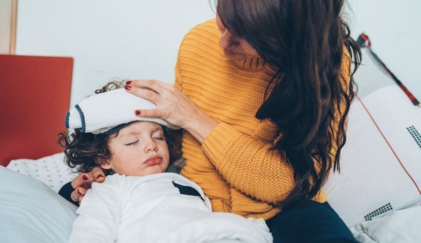 Une mère applique un cataplasme sur le front d'un petit garçon malade. 