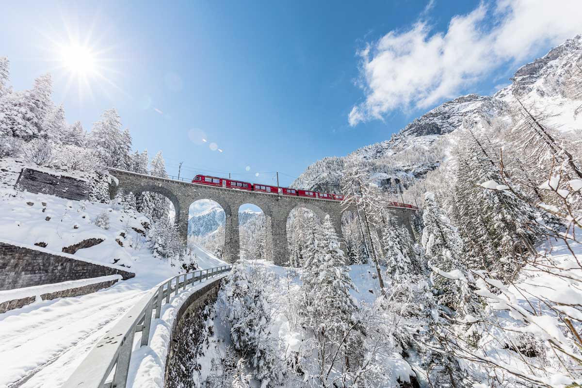 Die Rhätische Bahn fährt über das Albulaviadukt in der verschneiten Winterlandschaft.